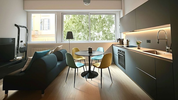 Una sala de estar moderna con un sofá, una mesa de comedor con sillas, un televisor y una zona de cocina con un fregadero y armarios.