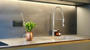 Una cocina moderna con un lavamanos de acero inoxidable, un florero de cobre con una planta verde y un grifo elegante.