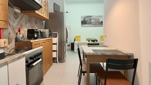 Une cuisine moderne équipée d’un four encastré, d’un four à micro-ondes et d’un réfrigérateur en acier inoxydable. On y trouve un coin repas avec une table et des chaises, ainsi qu’une petite plante accrochée au mur.