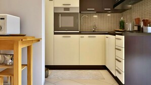 Una cocina moderna con armarios blancos y marrón oscuro, un microondas, un lavamanos y un salpicadero de azulejos.