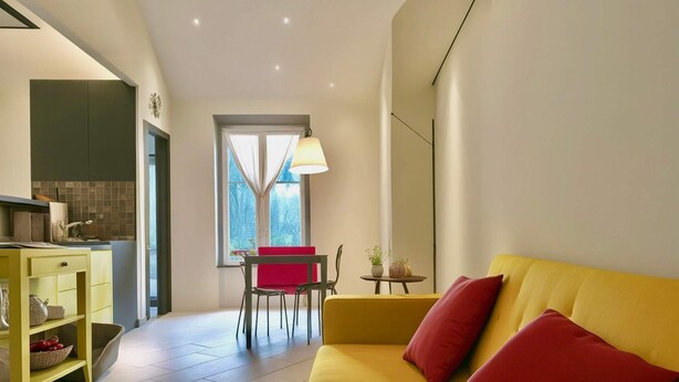 Una sala moderna con un sofá amarillo y cojines rojos, un comedor con una silla roja y una cocina con un mueble amarillo.