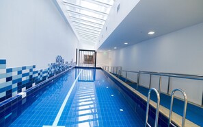 Swimmers can enjoy a refreshing dip in the pool surrounded by a blue-tiled wall and a plain white wall.