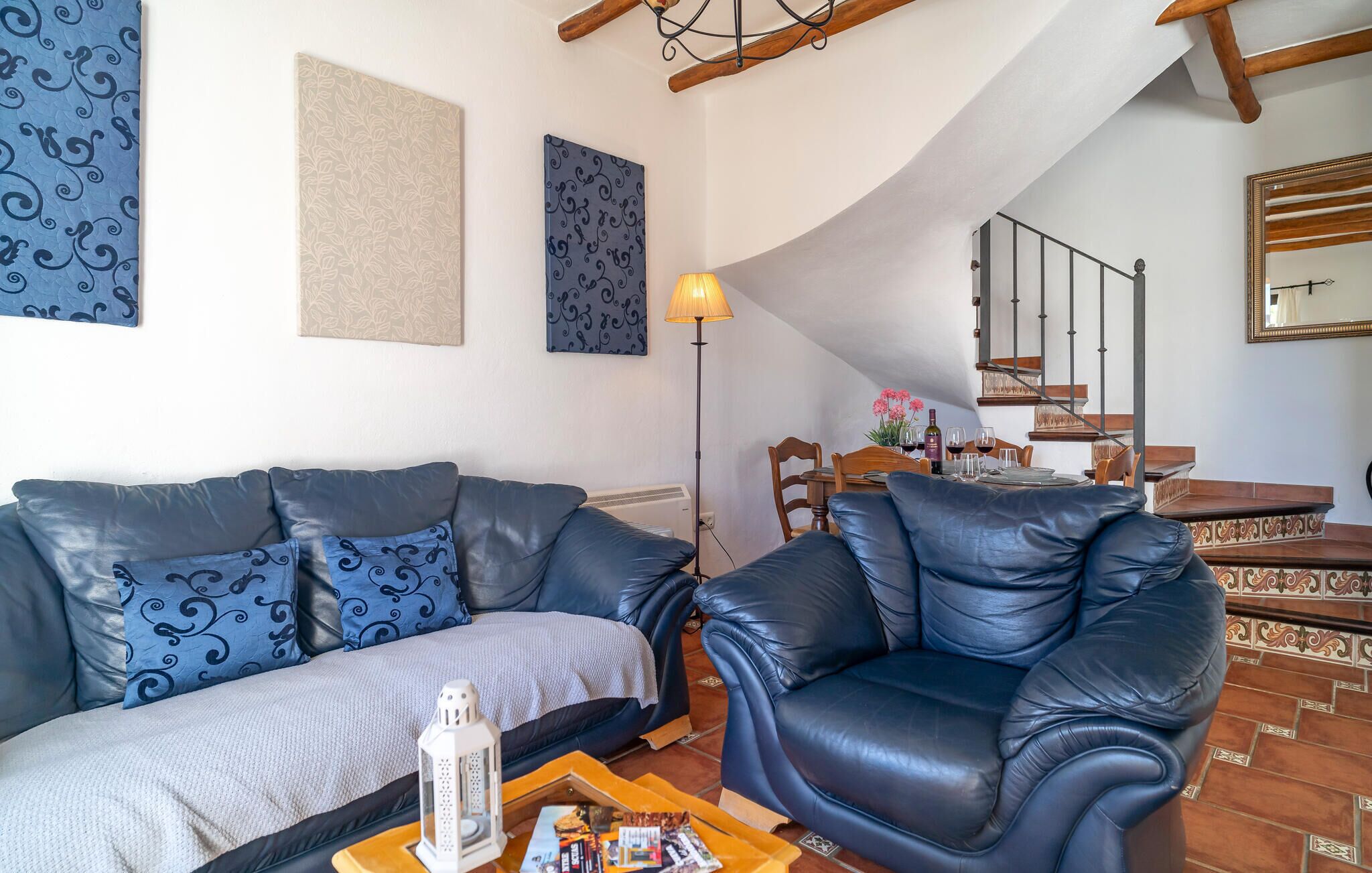 Ein Wohnzimmer mit Sofa und Sessel, einem Esstisch mit Stühlen, einer Treppe und einem Spiegel.