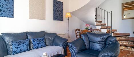 Ein Wohnzimmer mit Sofa und Sessel, einem Esstisch mit Stühlen, einer Treppe und einem Spiegel.