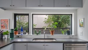 Une cuisine moderne dotée d’une grande fenêtre, d’un évier en acier inoxydable et de diverses plantes en pot.