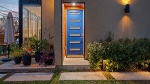 Une maison moderne avec une porte bleue, des plantes en pot et un paillasson.