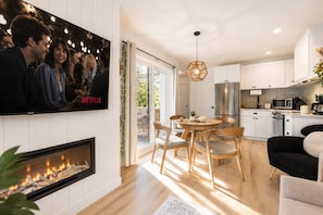 A modern kitchen with white cabinets, a stainless steel refrigerator, and a dining area with wooden chairs.