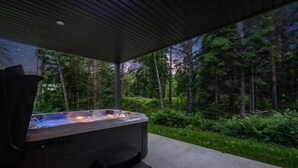A hot tub with steps, surrounded by a concrete deck and a forested area.