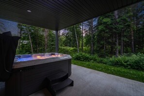 A hot tub with steps, surrounded by a concrete deck and a forested area.