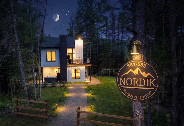 A Nordic Safari & Saloon lodge with a visible contact number, a well-lit exterior, and a path leading to the entrance.