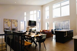A spacious living area with a dining table, black chairs, a sofa, and a kitchen island. - Spa, Mountains & Ultimate Comfort | Le Jameson (Saint-Philémon)