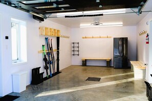 A garage with a concrete floor, a wooden bench, a black refrigerator, and a set of skis. - Spa, Mountains & Ultimate Comfort | Le Jameson (Saint-Philémon)