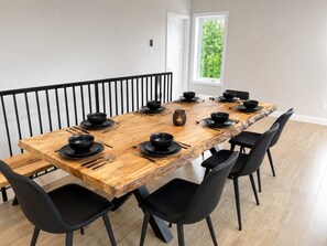 A dining area with a wooden table set for six, black chairs, and a window with a view of greenery. - Spa, Mountains & Ultimate Comfort | Le Jameson (Saint-Philémon)