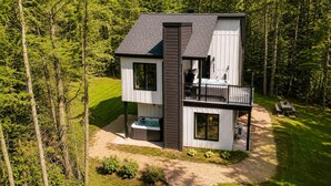 Eine moderne, zweistöckige Holzhütte mit Balkon, Whirlpool und Terrasse.