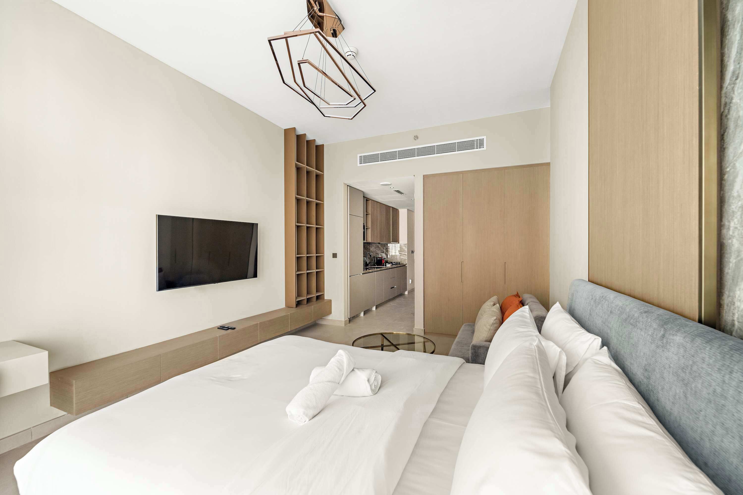 Habitació d'hotel moderna amb un llit gran, televisió de pantalla plana, armari integrat i una cuineta de fons.