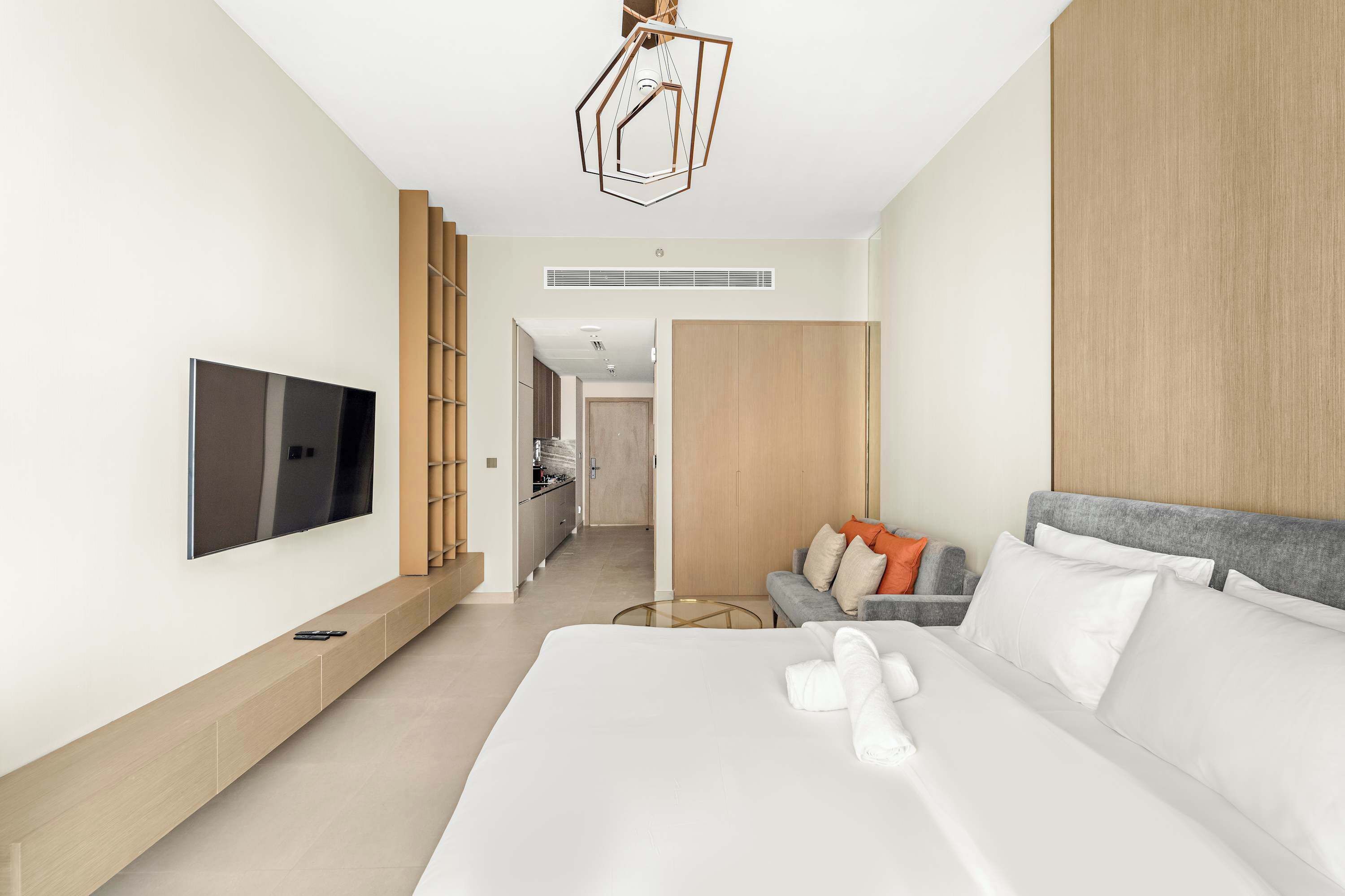 A modern hotel room with a large bed, a flat-screen TV mounted on the wall, a sofa, and a staircase leading to other rooms.