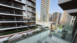 A modern building with multiple balconies, a glass facade, and a view of a cityscape with high-rise buildings.