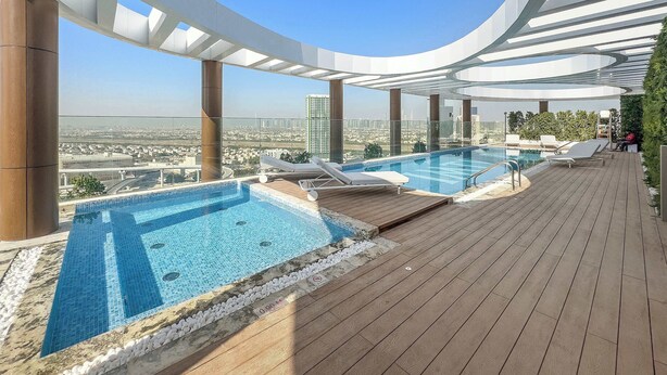 A rooftop pool with a clear view of the cityscape, lounge chairs, and a wooden deck.