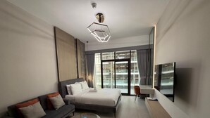 A modern hotel room with a bed, sofa, TV, and large windows.