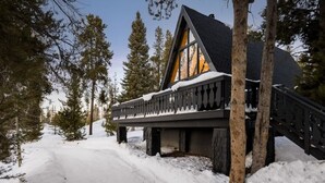 A cabin with a balcony, surrounded by snow and trees.