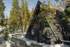 A cabin with a steep roof, surrounded by trees and snow.