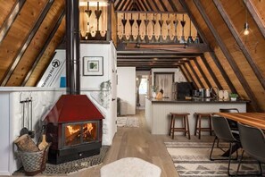 A loft-style room with a wood-burning stove, a kitchen area, and a dining space. - Charming Rocky Mountain A-Frame (Fraser)