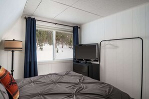 A bedroom with a bed, a TV, a dresser, a window with curtains, and a coat rack.