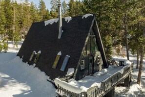 A snow-covered wooden cabin with a steep roof, a chimney, and a small porch.