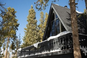 A cabin with a steeply pitched roof, large windows, and a snow-covered deck.