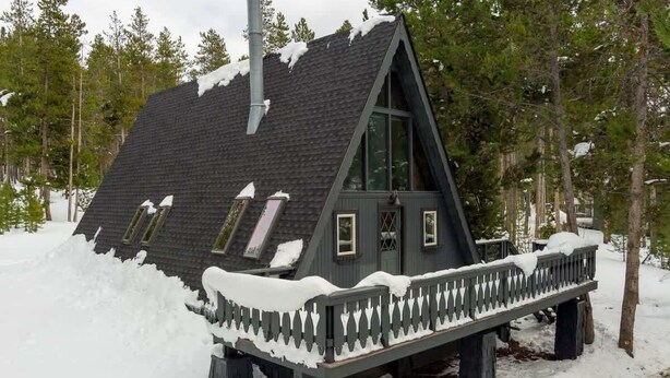 A cabin with a steep roof, a deck with a railing, and a chimney.