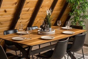 A dining table set with plates, glasses, and a centerpiece in a room with wooden walls and a plant. - Charming Rocky Mountain A-Frame (Fraser)