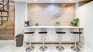 Une cuisine avec un mur en briques, des meubles blancs et quatre tabourets de bar.