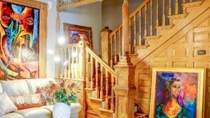 Un salon avec un escalier, un canapé, une table basse en verre et deux tableaux.