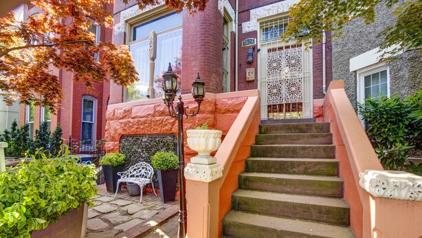 A brick building with a staircase leading to a second-floor entrance, a white gate, and a small outdoor seating area with chairs and a table. - Logan Mansion Suite 2 2 Bedroom Apartment Hotel (Washington)