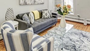 A modern living room with a grey sofa, striped armchairs, a glass coffee table, and a floral vase. - Logan Mansion Suite 4 2 Bedroom Apartment Hotel (Washington)