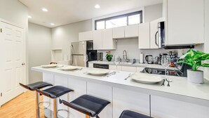 A modern kitchen with white cabinets, a central island with bar stools, and a large window above the sink. - Logan Mansion Suite 4 2 Bedroom Apartment Hotel (Washington)
