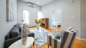 A modern living room with a grey sofa, striped armchair, and a glass coffee table. There is a wooden cabinet and a bed in the background. - Logan Mansion Suite 4 2 Bedroom Apartment Hotel (Washington)