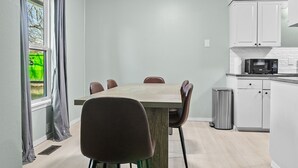 A modern kitchen with white cabinets, a microwave, and a dining area with a wooden table and chairs. - Charming Pastel Duplex in the Heart of Tulsa (Tulsa)