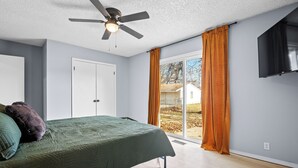 A bedroom with a bed, ceiling fan, sliding glass doors, and a TV mounted on the wall. - Charming Pastel Duplex in the Heart of Tulsa (Tulsa)
