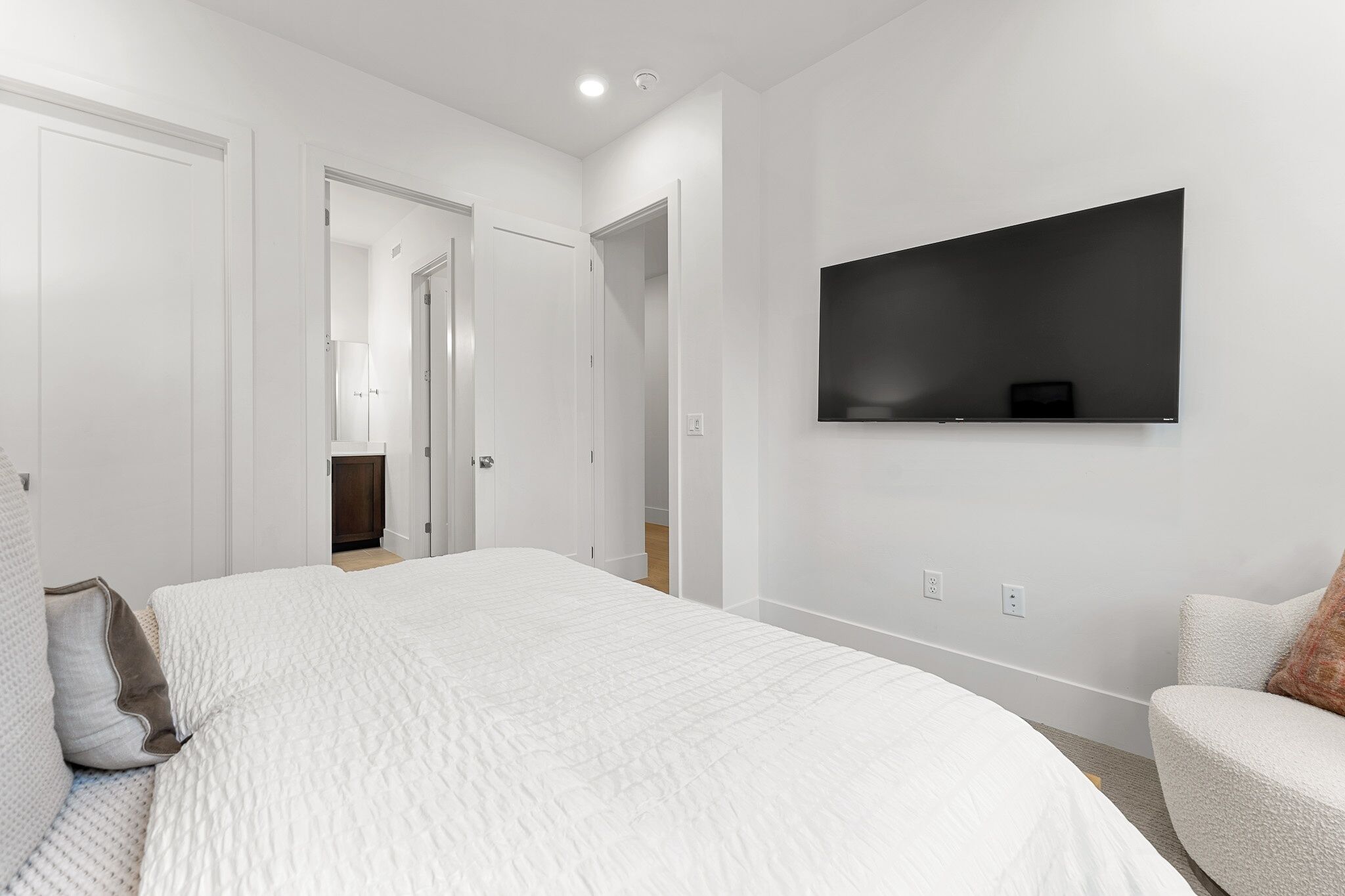 A modern bedroom with a large bed, a mounted TV, and a chair.