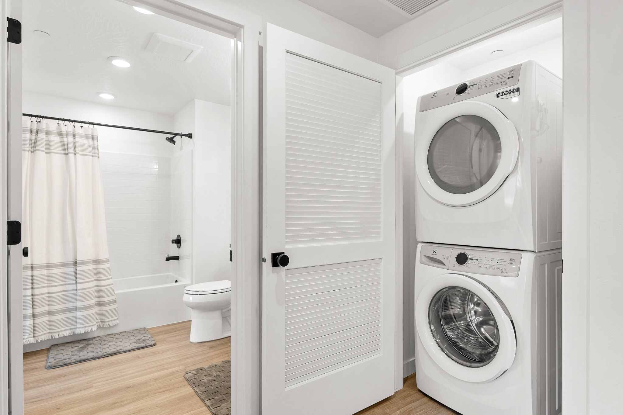 A modern bathroom with a shower, toilet, and a stacked washer and dryer.