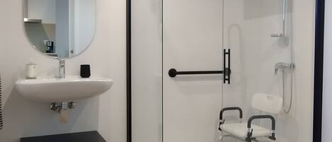 A modern bathroom with a glass-enclosed shower, a white sink, and a black storage unit.