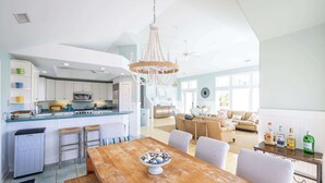 A spacious kitchen with white cabinets, a wooden dining table, and a chandelier. - Newly Renovated! Semi Oceanfront w/ Pool & Hot Tub (Duck)