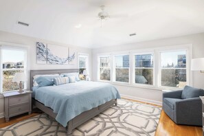 Une chambre à coucher avec un lit, une table de chevet, une chaise et de grandes fenêtres.