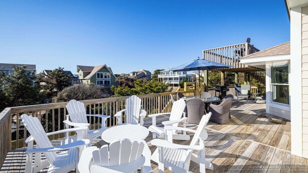 A deck with white Adirondack chairs and a table, overlooking a residential area with houses and trees. - Newly Renovated! Semi Oceanfront w/ Pool & Hot Tub (Duck)