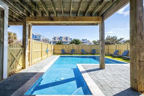 Une piscine rectangulaire dotée d’une terrasse en bois et d’un espace abrité.