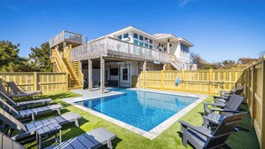 A backyard with a swimming pool, lounge chairs, and a two-story house with a balcony. - Newly Renovated! Semi Oceanfront w/ Pool & Hot Tub (Duck)
