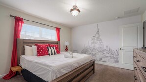 Ein Schlafzimmer mit einem hölzernen Bett, roten Vorhängen, einer weißen Wand mit einer Schlossmalerei, einem Nachttisch mit Lampe und einer Kommode.