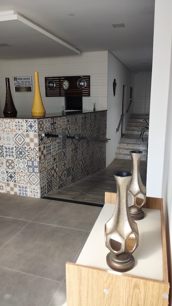 Un vestíbulo de hotel con una pared de azulejos, una mesa de recepción y una escalera que conduce a los pisos superiores.