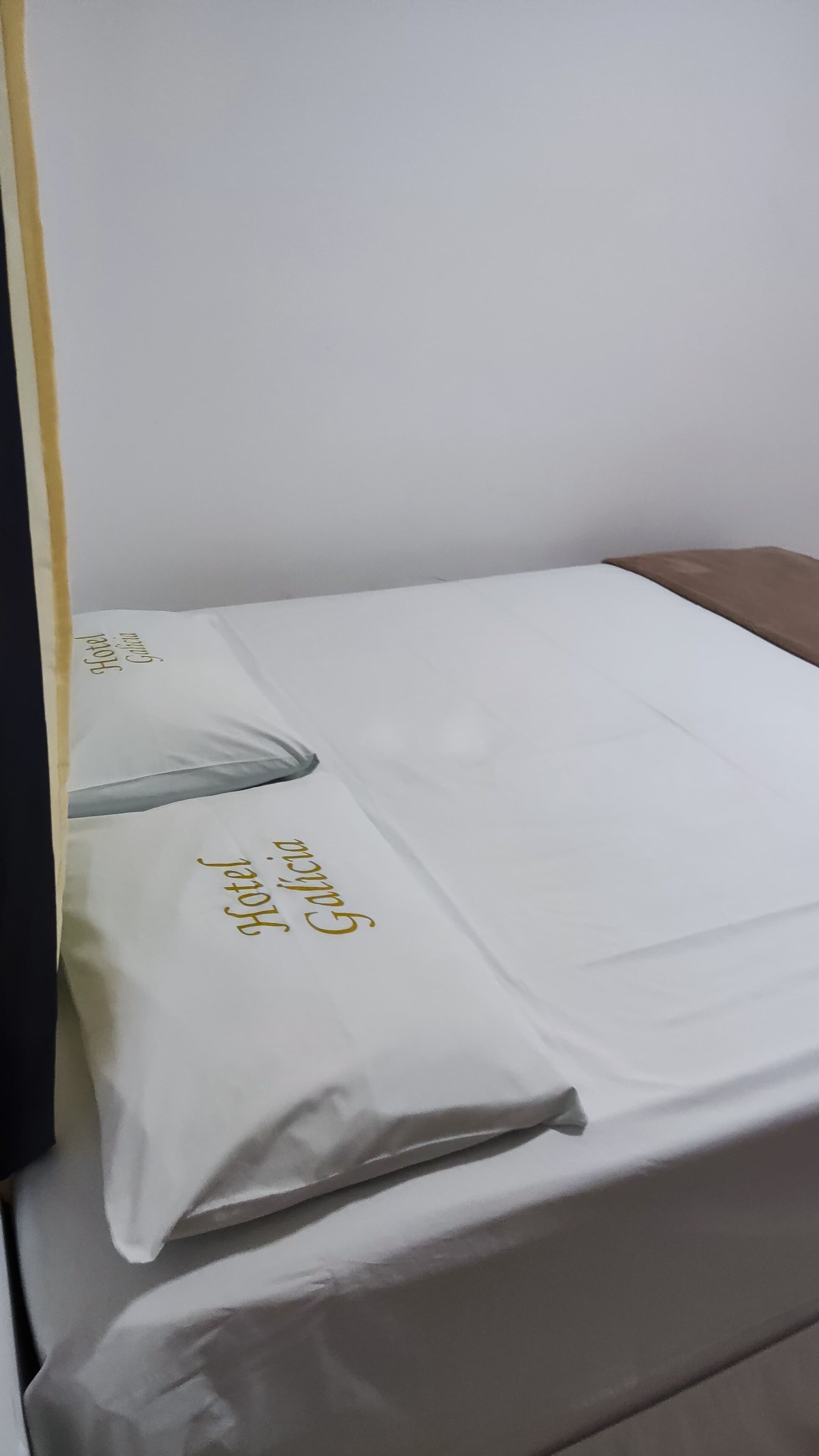 A hotel bed with a white mattress and a pillow with gold text.
